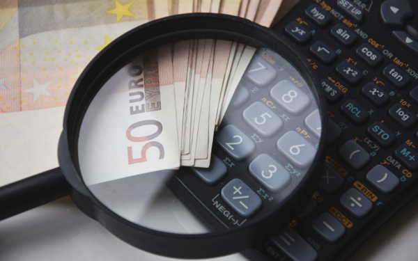 Euro bills under magnifying glass with calculator, symbolizing finance and analysis.