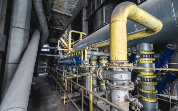 Close-up of an intricate industrial pipeline system featuring yellow valves and steel structures inside a factory.